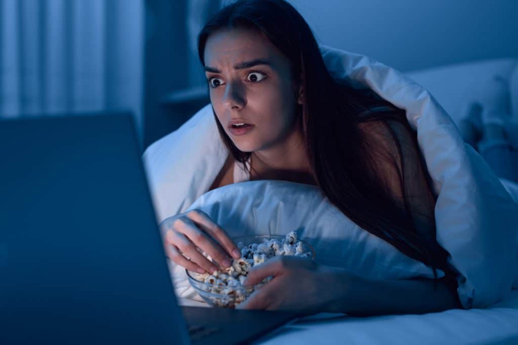 Amazed Female Eating Popcorn And Watching Horror Movie On Laptop