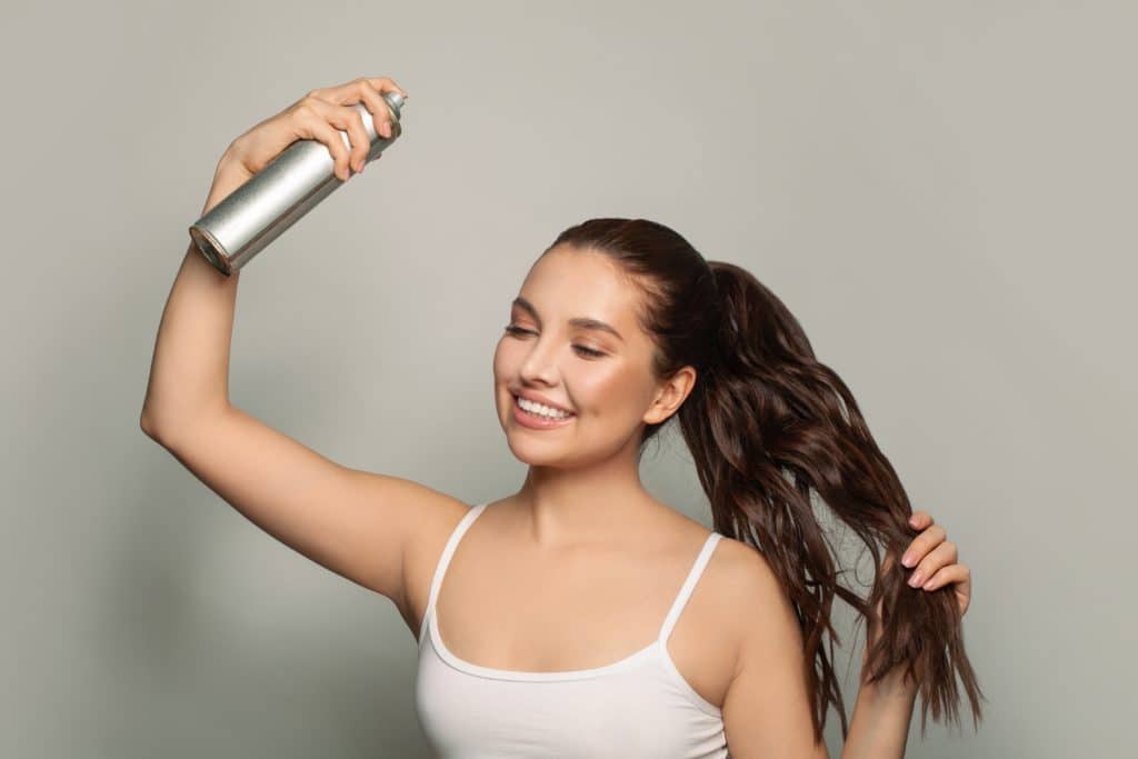 Beautiful Young Woman Applying Hair Spray On Her Hair.