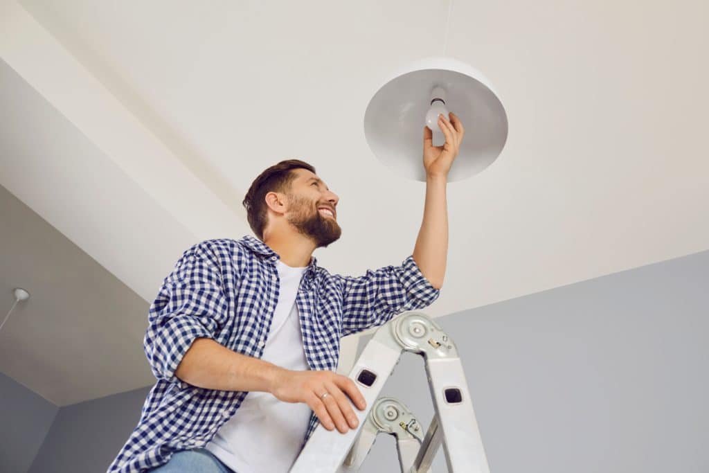 Happy Man Changing A Light Bulb At Home. High Angle