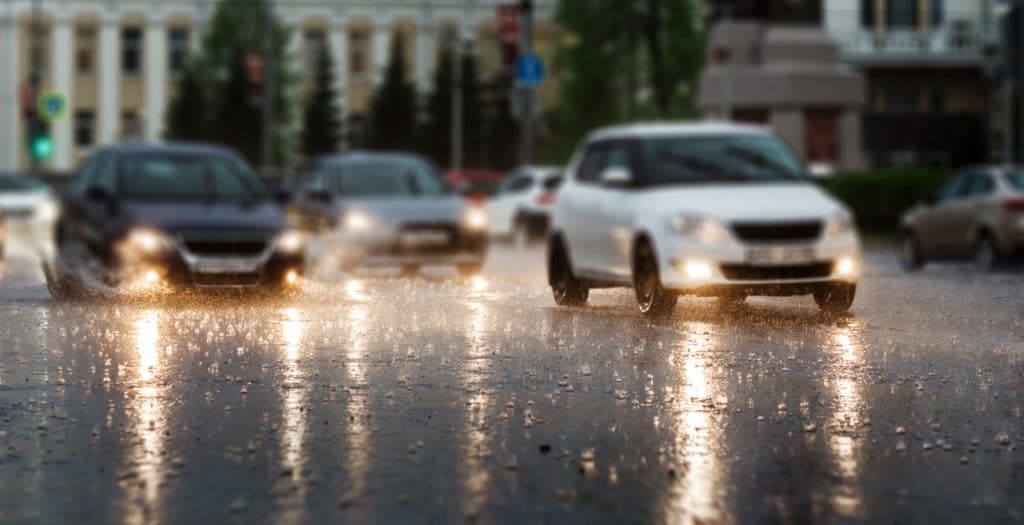 Heavy Rain Hitting A Concrete Sidewalk While Cars Drive By.