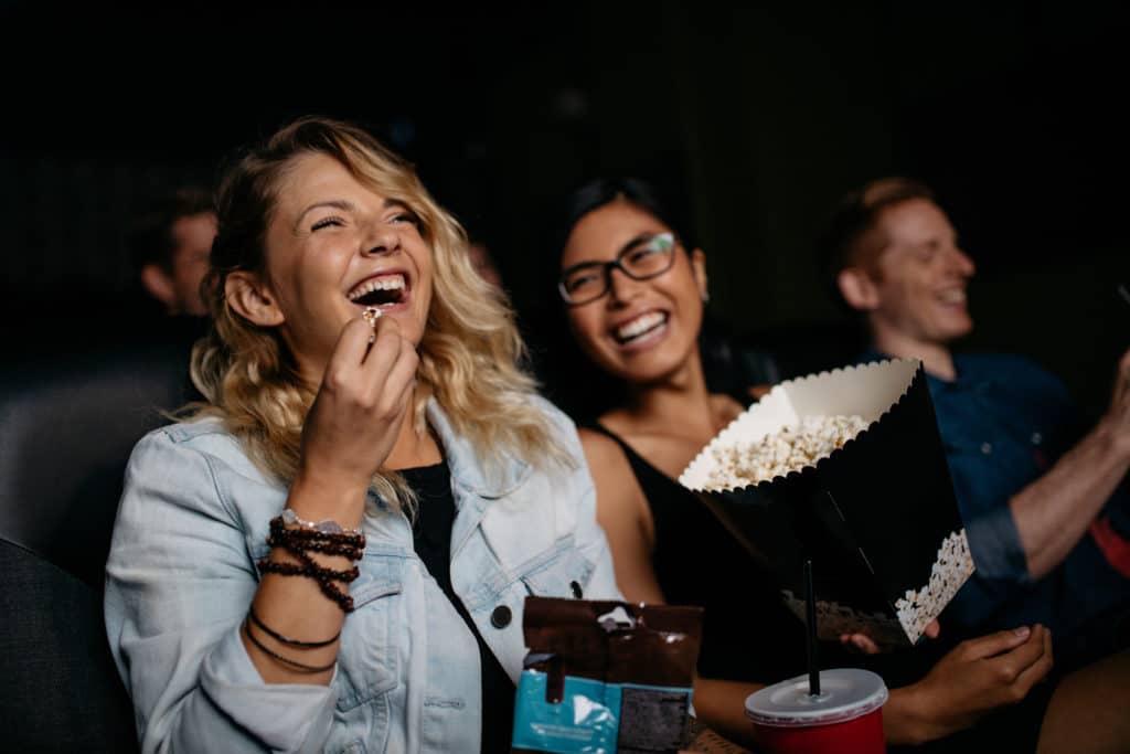 Young Woman With Friends Watching Movie In Cinema And Laughing.