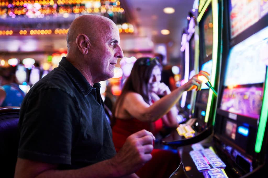 Elderly Tourist Playing Slot Machines And Gambling In Casino