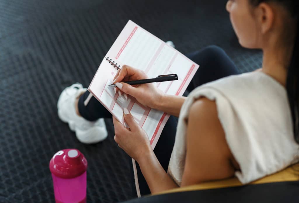 Workout Planning. Young Woman Making Her Workout Schedule In Notebook