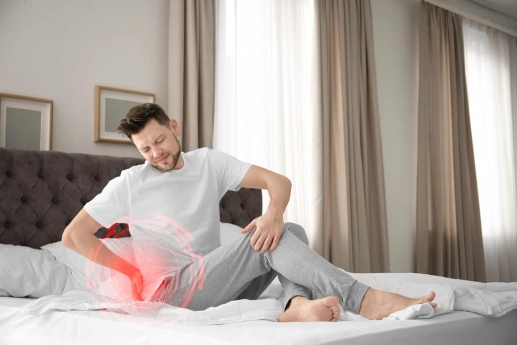 Man Suffering From Back Pain After Sleeping On Uncomfortable Mattress