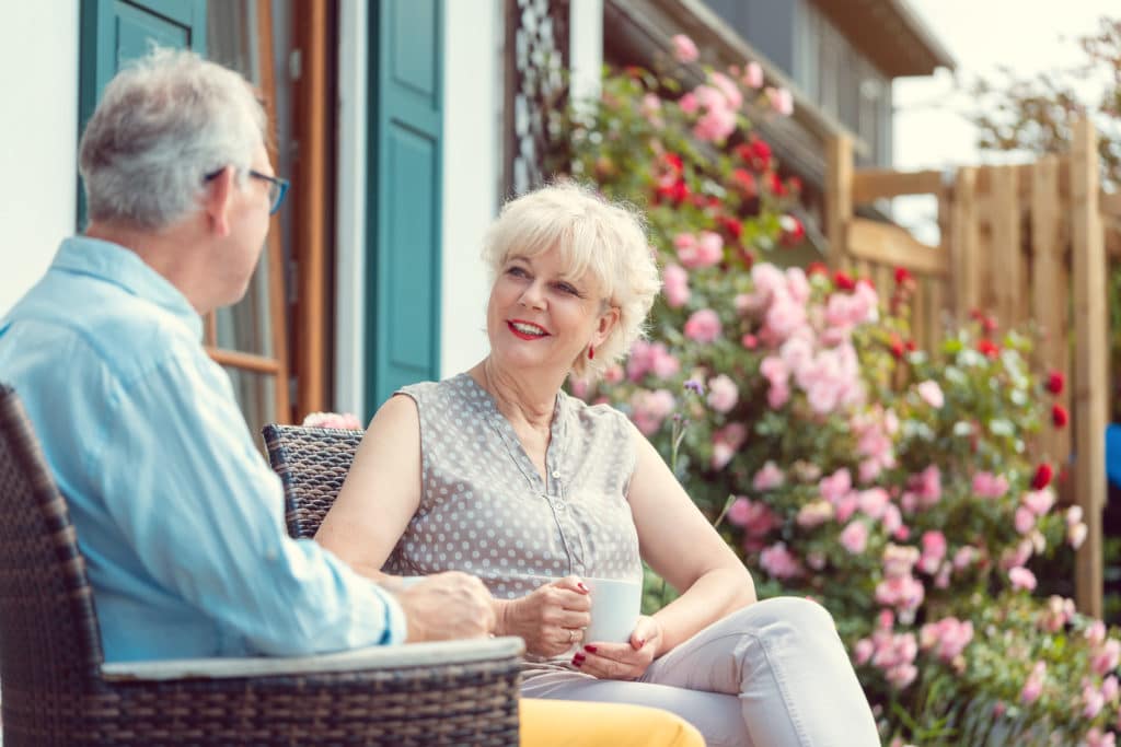 Senior Couple Enjoying Their Coffee Sitting On Porch In Front