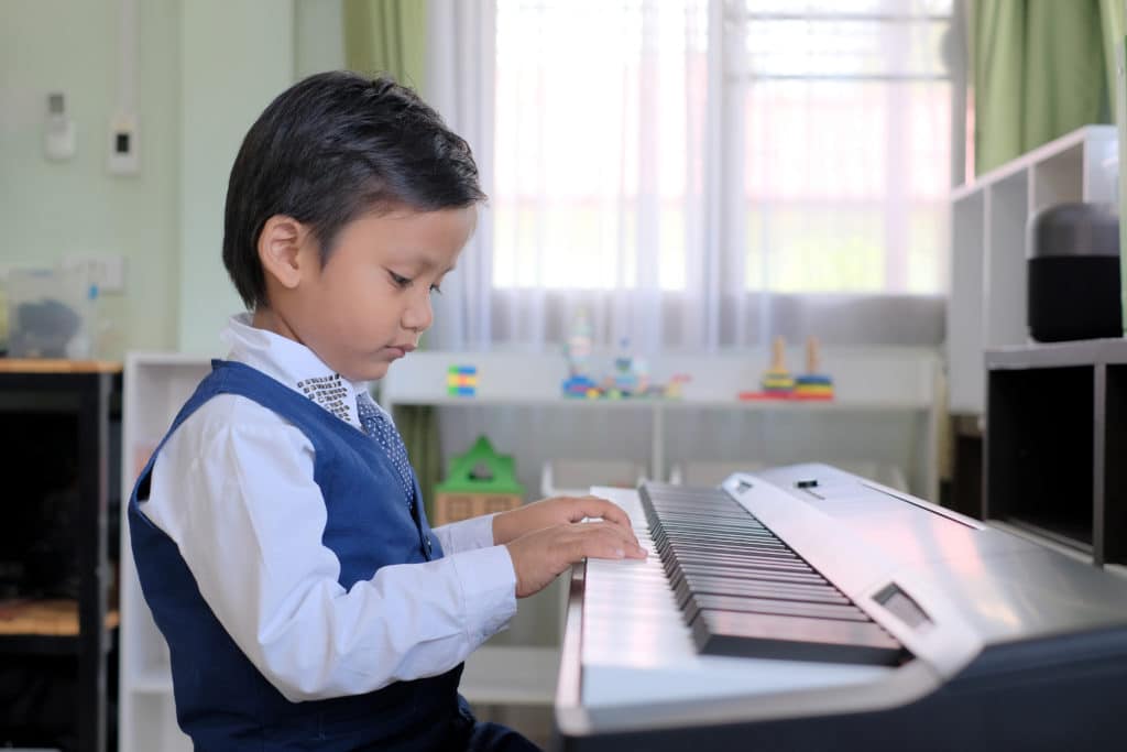 Portrait Of Adorable Young Asian Kid Practicing The Piano Alone