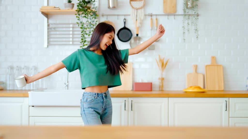 Asian Young Woman Dancing In Kitchen Room. Female Happy And