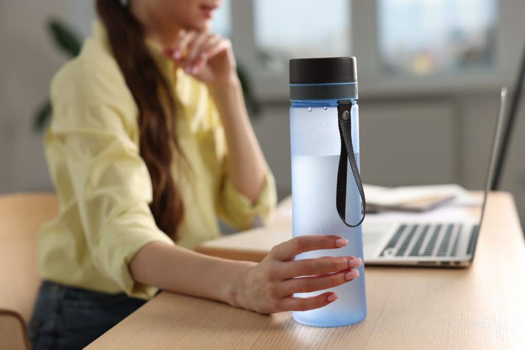 Woman Holding Transparent Bottle At Workplace Indoors Closeup