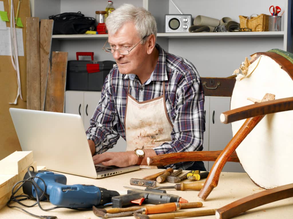 Portrait Of Retired Carpenter Sitting At His Workshop And Working