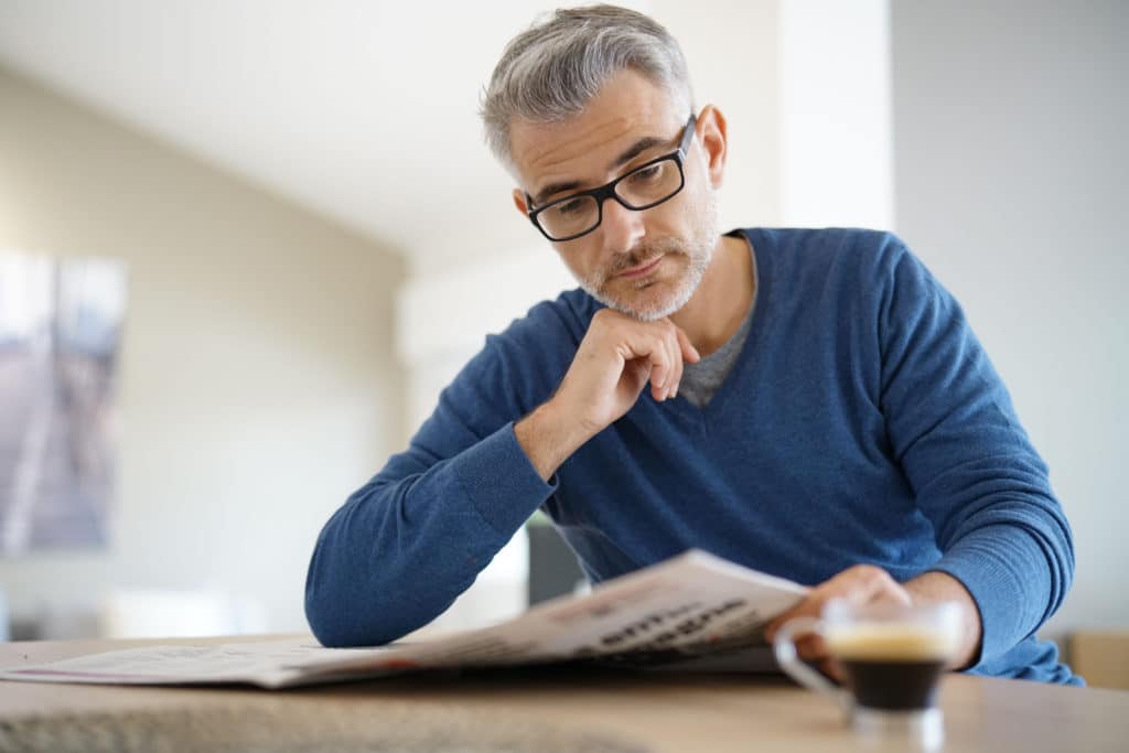 Middle Aged Man At Home Drinking Coffee And Reading Newspaper