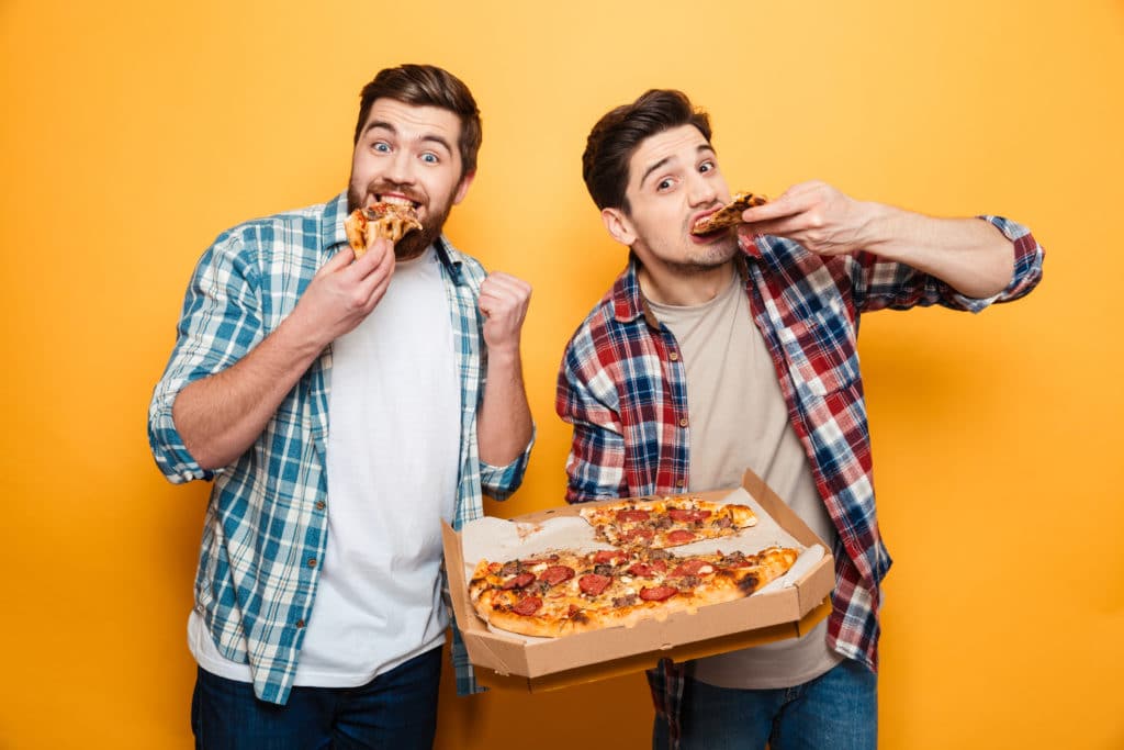 Two Cheerful Men In Shirts Eating Pizza And Looking At