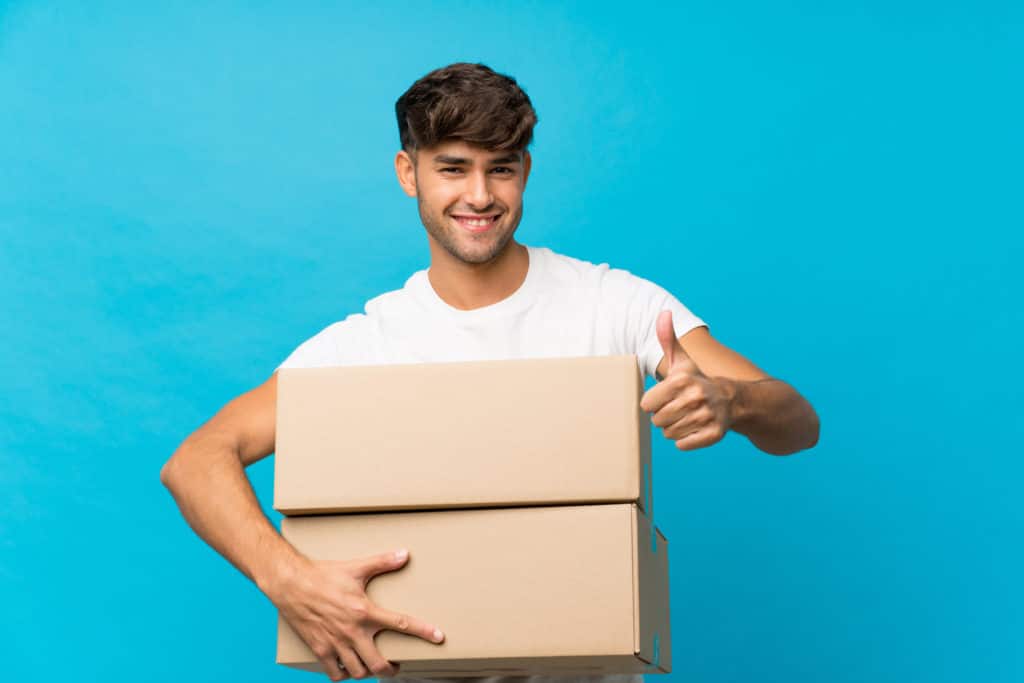 Young Handsome Man Over Isolated Blue Background Holding A Box