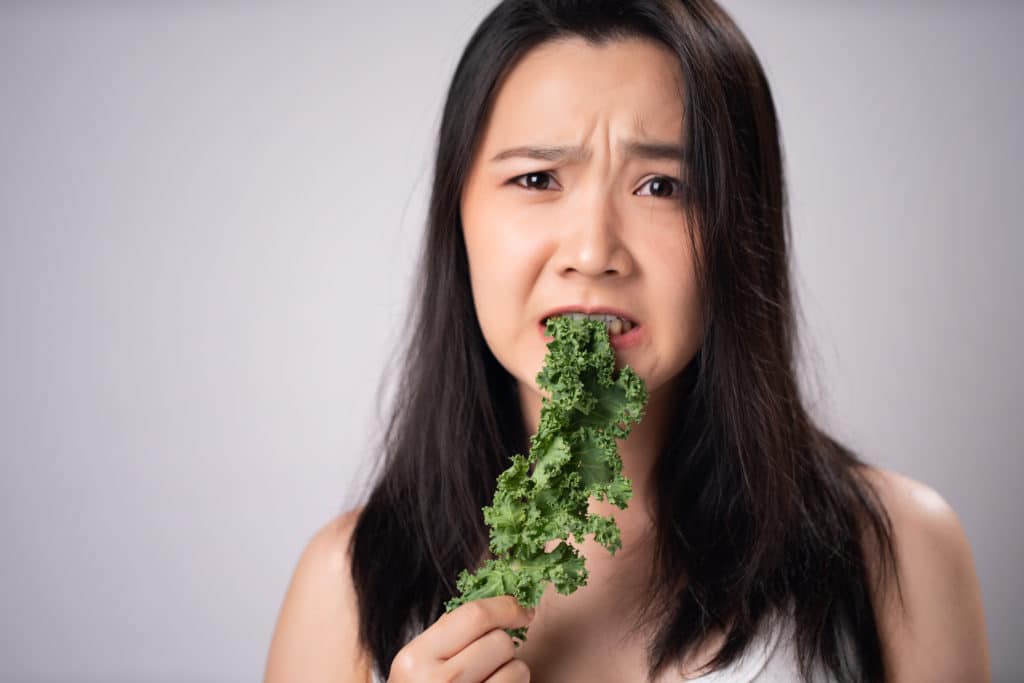 Asian Woman Trying To Kale For Diet Isolated Over White