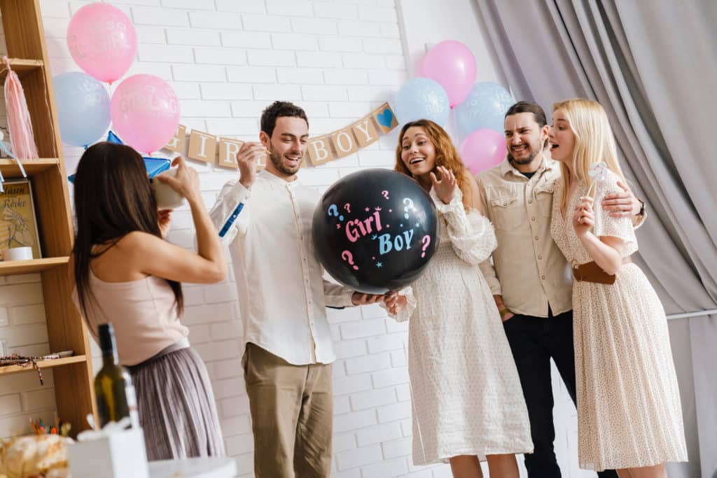 Young Excited Couple Blowing Up Surprise Balloon During Gender Reveal