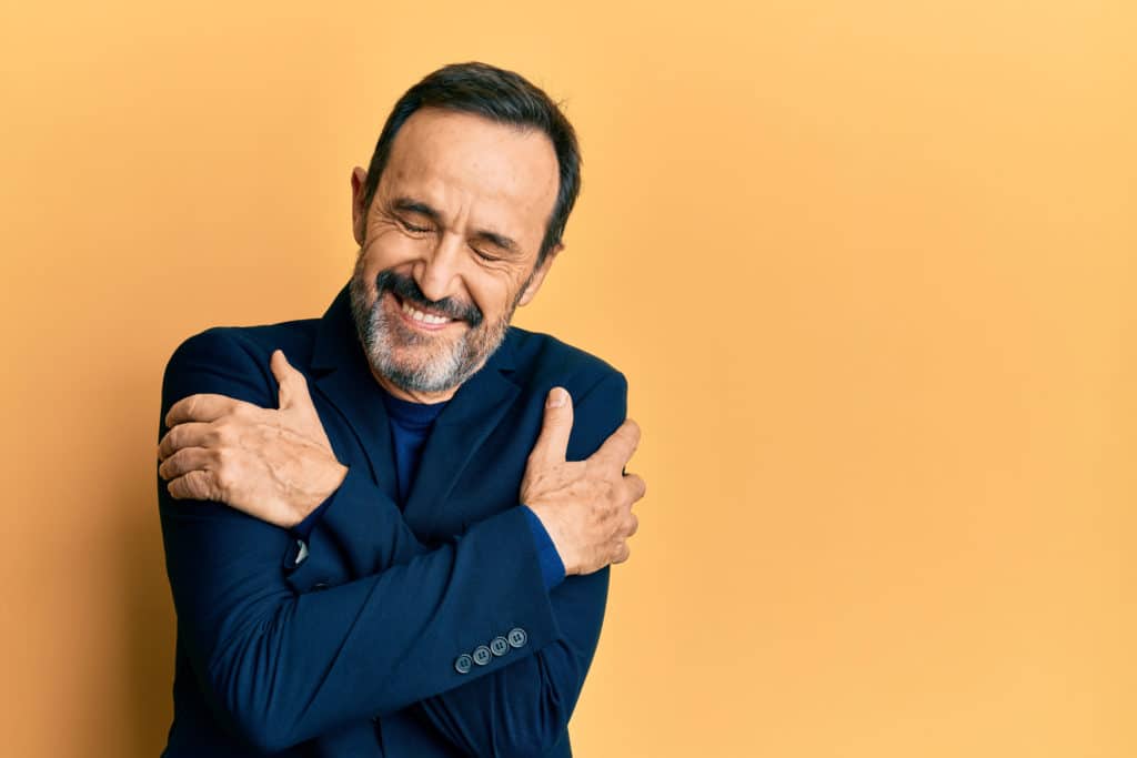 Middle Age Hispanic Man Wearing Business Clothes Hugging Oneself Happy