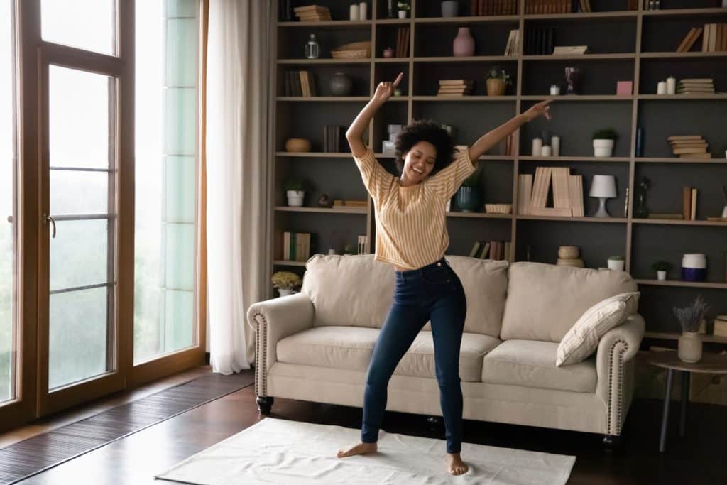 Happy Carefree Young African American Woman Dancing On Floor Carpet 