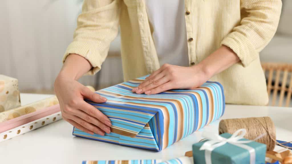 Woman Wrapping Gift At White Table Indoors Closeup