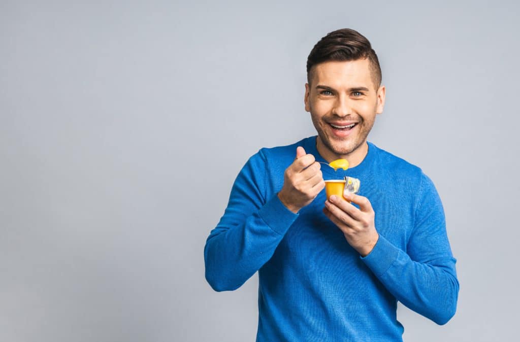Happy Young Ukrainian Handsome Man Eating Yogurt Isolated Over Grey