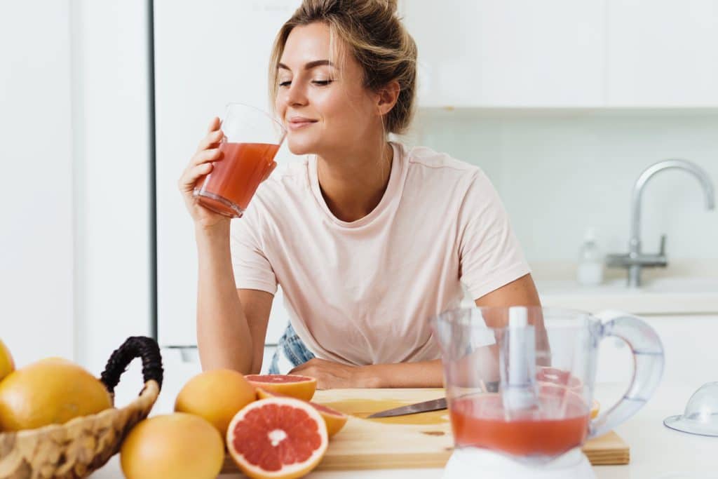 Young Woman Drinking Freshly Squeezed Homemade Grapefruit Juice In White