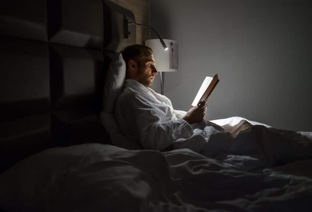 Midle Aged Caucasian Man Relaxing In Bed Reading Bestseller Novel Paper