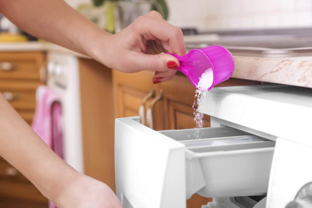 Woman Throws Laundry Detergent Into The Washing Machine Close Up.