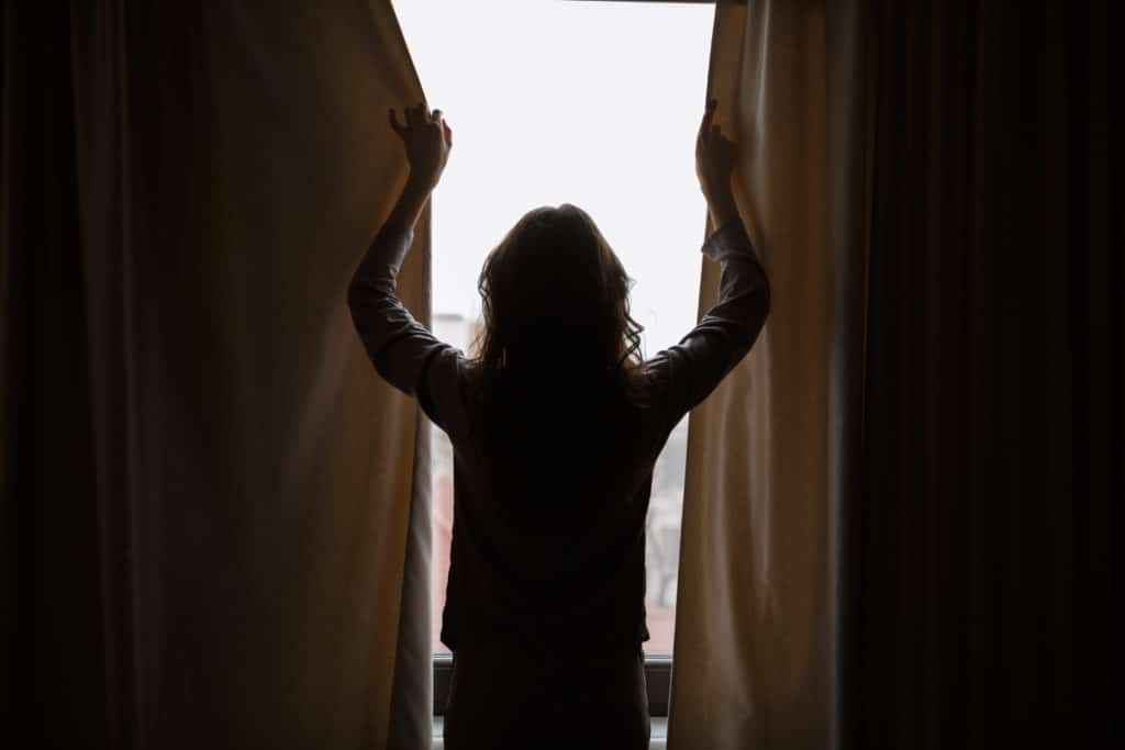 Silhouette Of Woman Which Closes Curtains. Back View