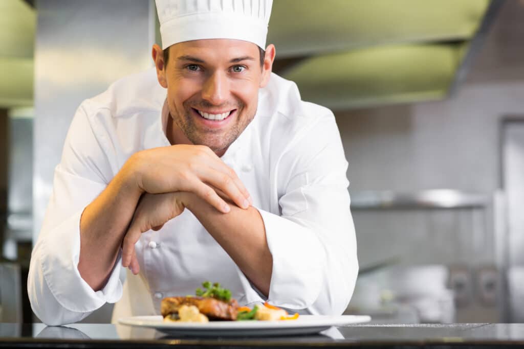 Portrait Of A Smiling Male Chef With Cooked Food Standing