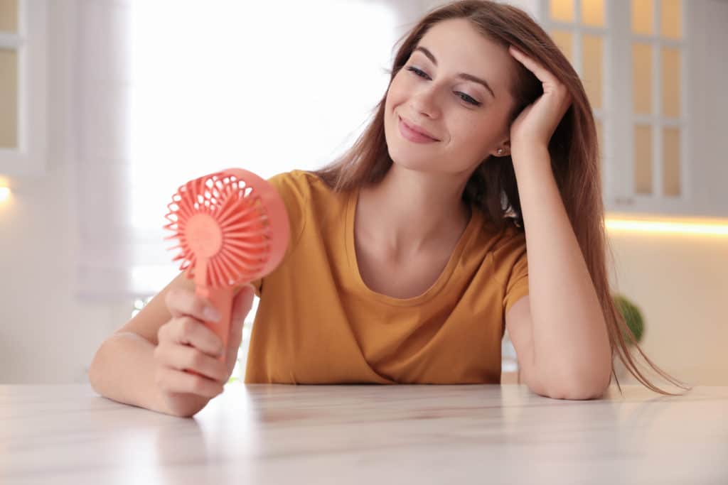 Woman Enjoying Air Flow From Portable Fan At Table In