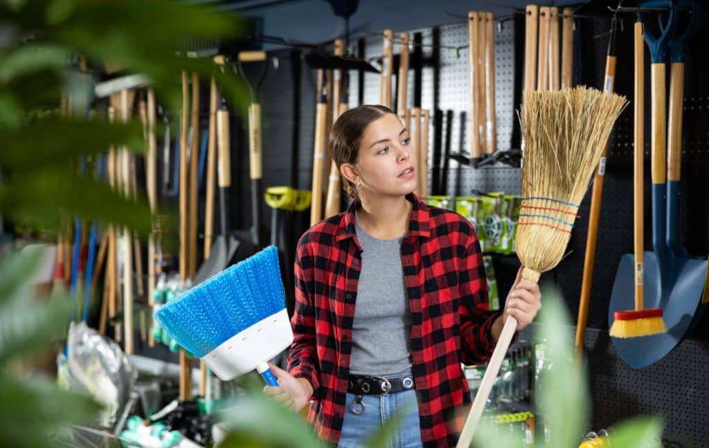Smiling Casual Young Woman Holding Two Brooms In Her Hands