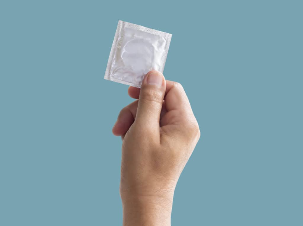 Foil Pack Of Condom In Male Hand Isolated On Turquoise