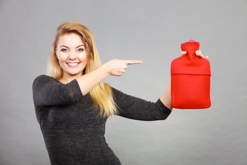 Positive Smiling Woman Recommending Warm Hot Water Bottle In Red