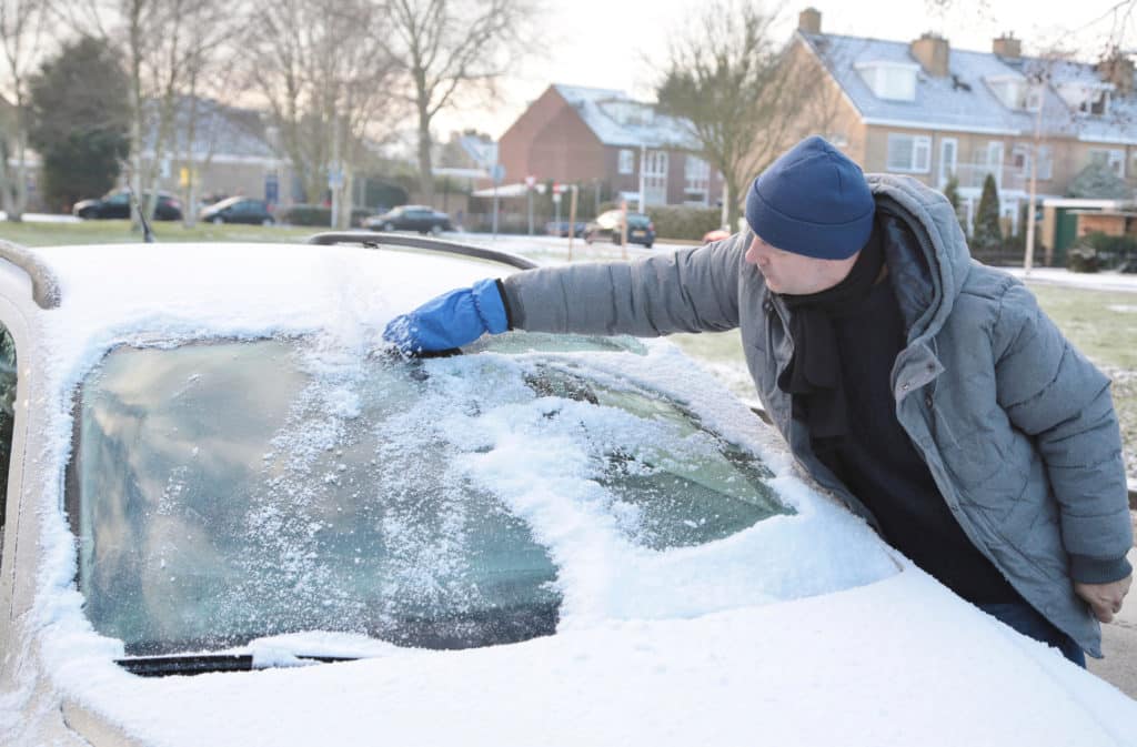 A Man Is Cleaning His Car With An Ice Scraper