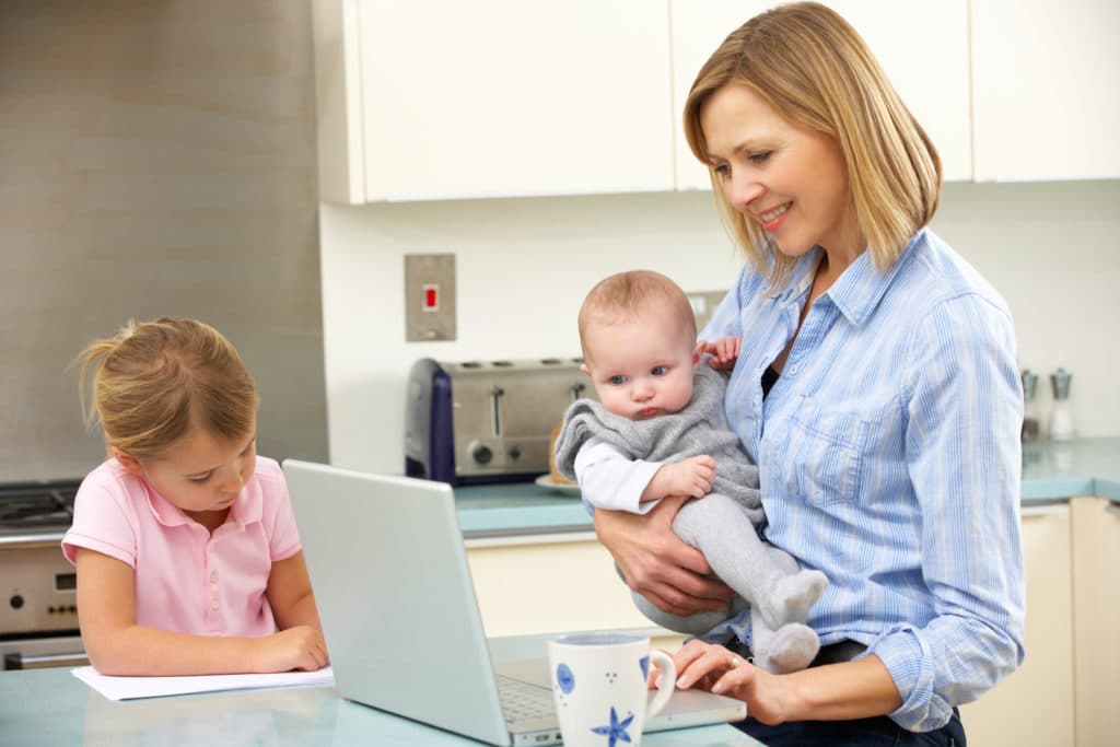 Mother With Children Using Laptop In Kitchen