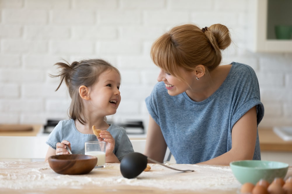 Smiling Mother Looking At Little Daughter And Feeding Her After