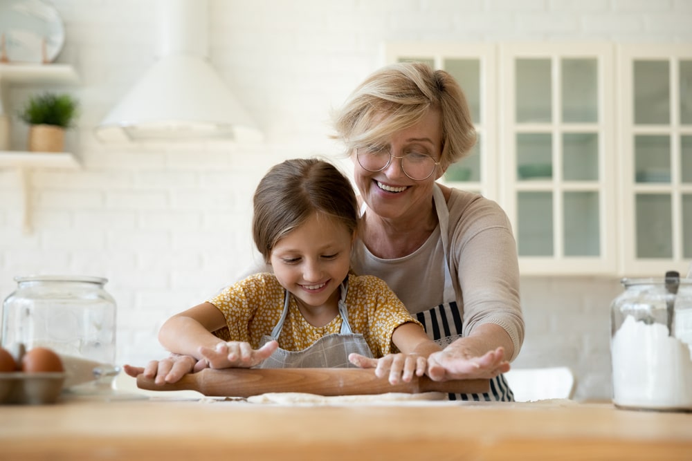 Happy Mature Grandmother Teaching Adorable Little Granddaughter To Rolling Dough